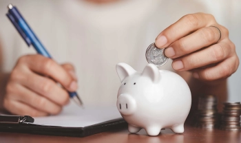 Sparschwein auf dem Tisch. Person mit Stift und Geld in der Hand, die Geld in das Schwein wirft